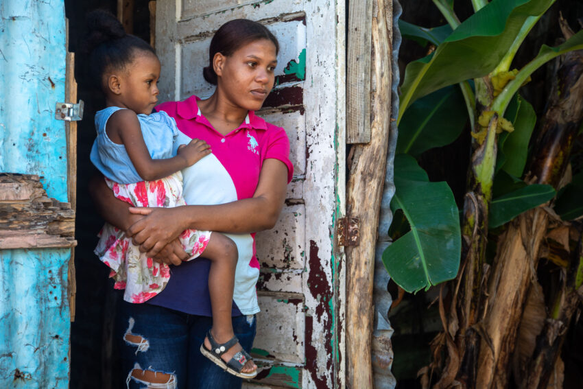 Mother and daughter stand outside the door of their home.