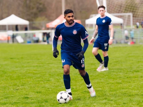 Male soccer player at the forefront focused on passing the ball, as his teammate stands behind him watching the play.