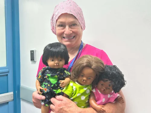 Female medical volunteer for Operation Smile Canada holding 3 cleft dolls