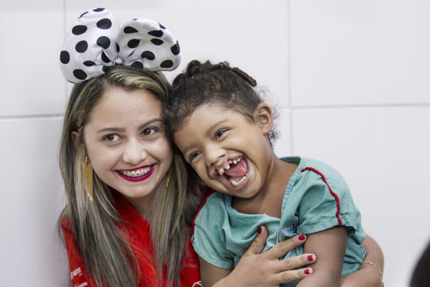 A woman smiles while holding a child with a cleft lip