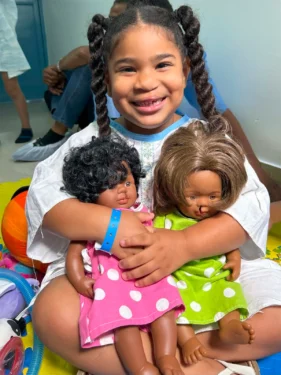 A young girl holding 2 cleft dolls
