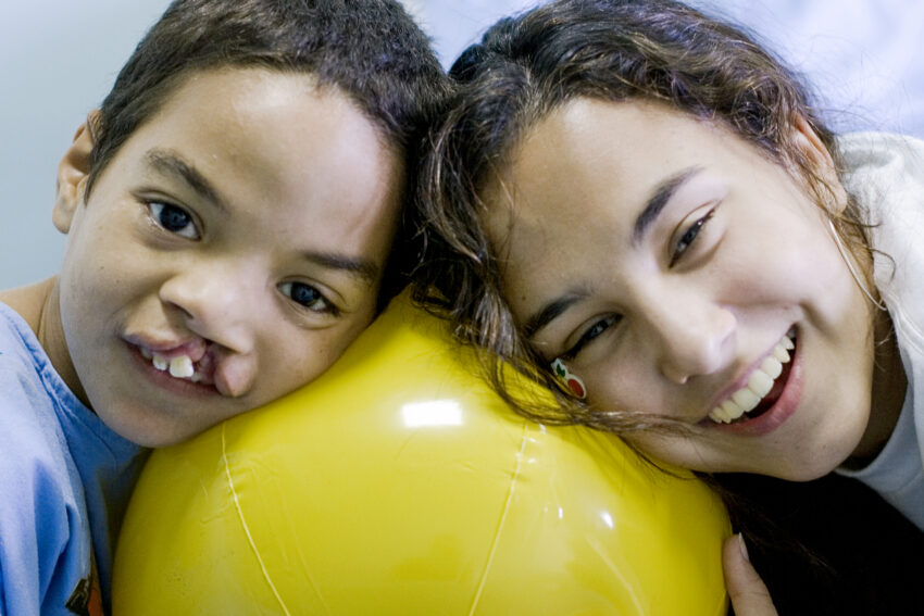 Young boy with cleft condition and woman lean on yellow ball while smiling