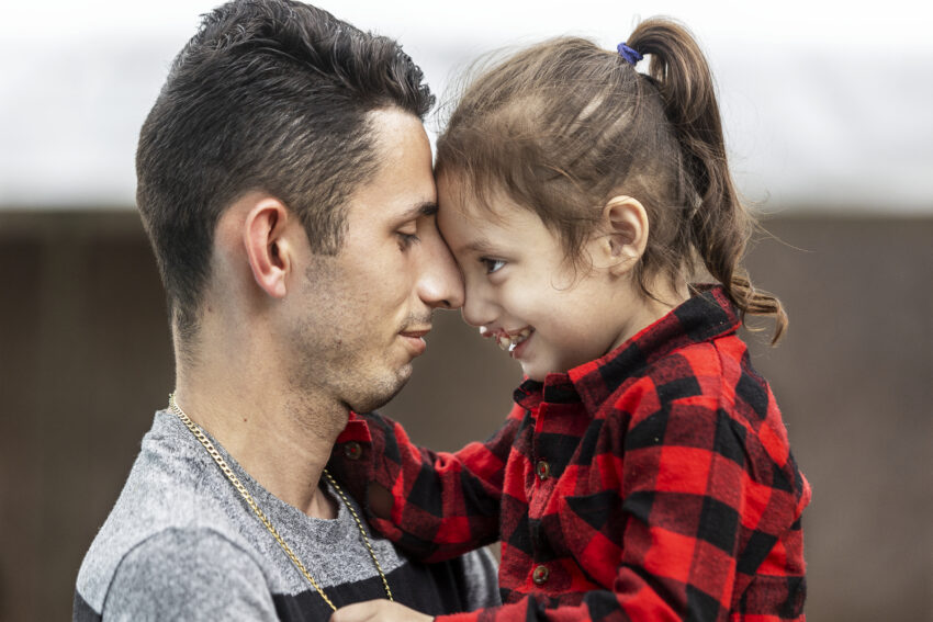 A man and his toddler daughter pose nose to nose with smiles on their faces.
