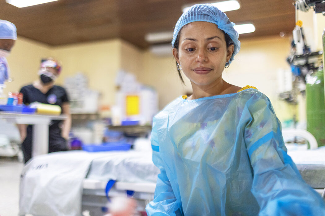 A woman wearing a surgical cap and gown looks down at a hospital bed.