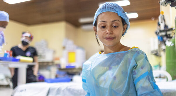 A woman wearing a surgical cap and gown looks down at a hospital bed.
