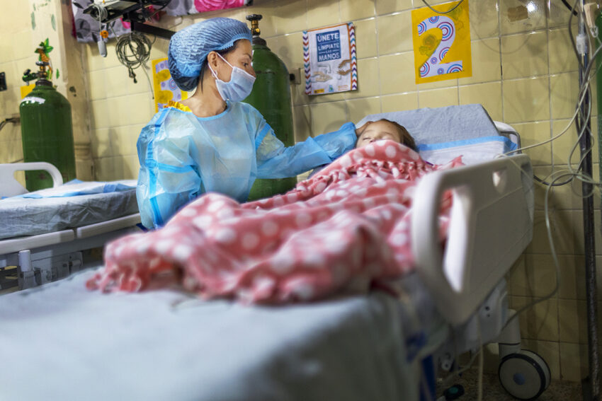 A mother looks at her sleeping daughter and rubs her head after surgery.
