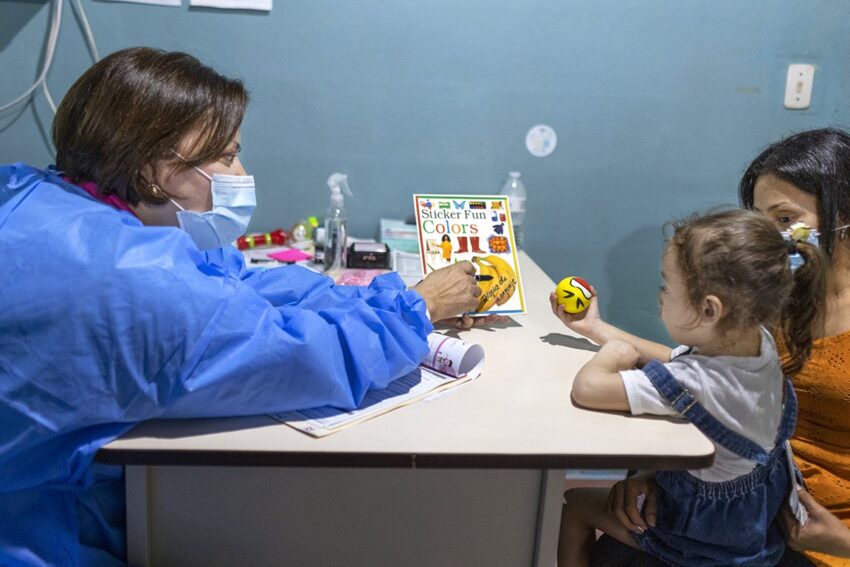 A medical professional sits with a child at a table.