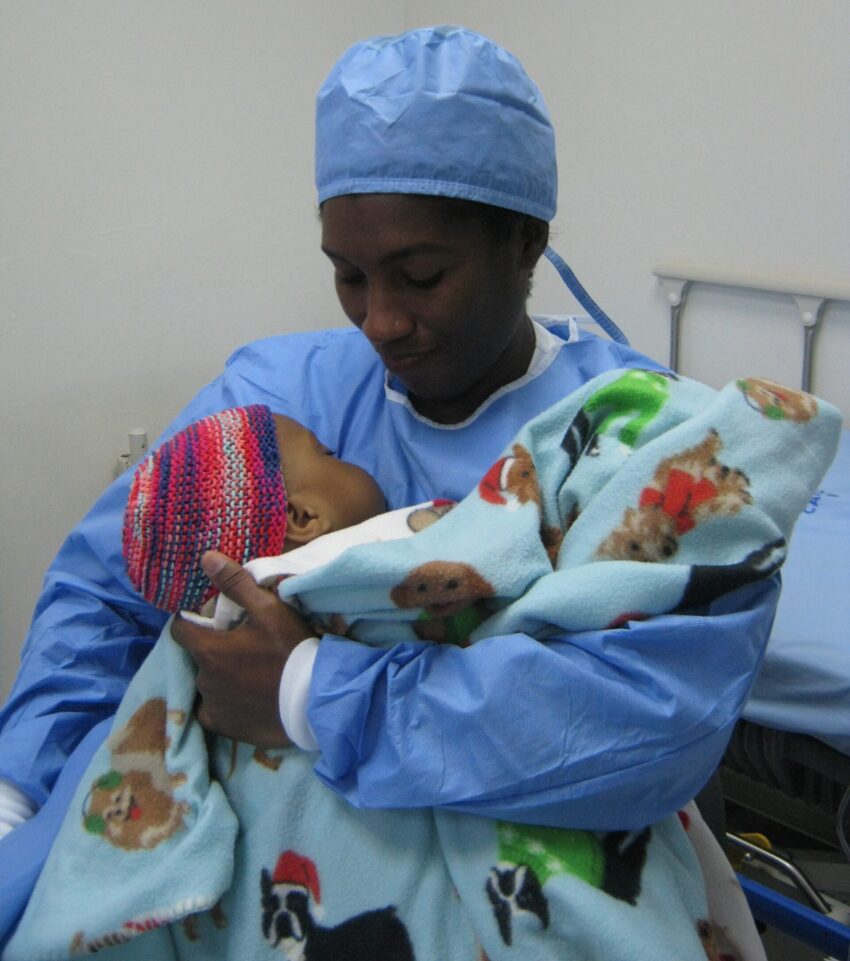 Mother wears surgical scrubs and holds her child after surgery.