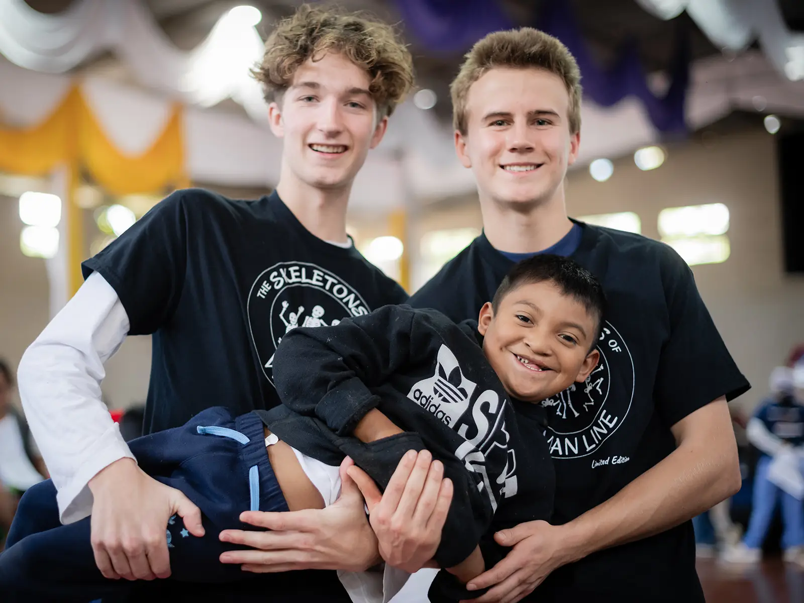 Two male teenagers hold up a child to pose for a photo