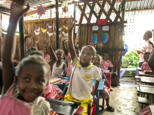 Children in a classroom in Madagascar raise their hands enthusiastically to answer a question.