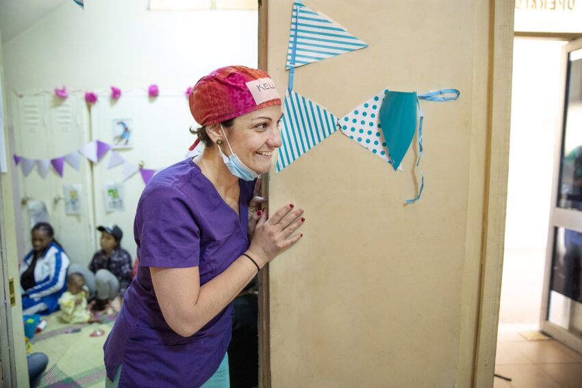 A woman in scrubs rounds the corner with a smile on her face.