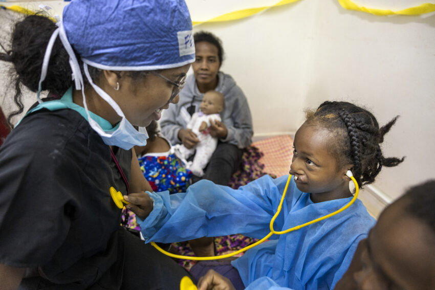 Girl with cleft uses stethescope on nurse preparing her for surgery.