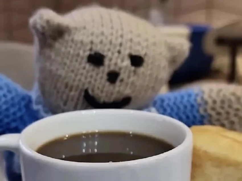 A teddy bear is seen looking into a cup of coffee that he is supposed to be drinking