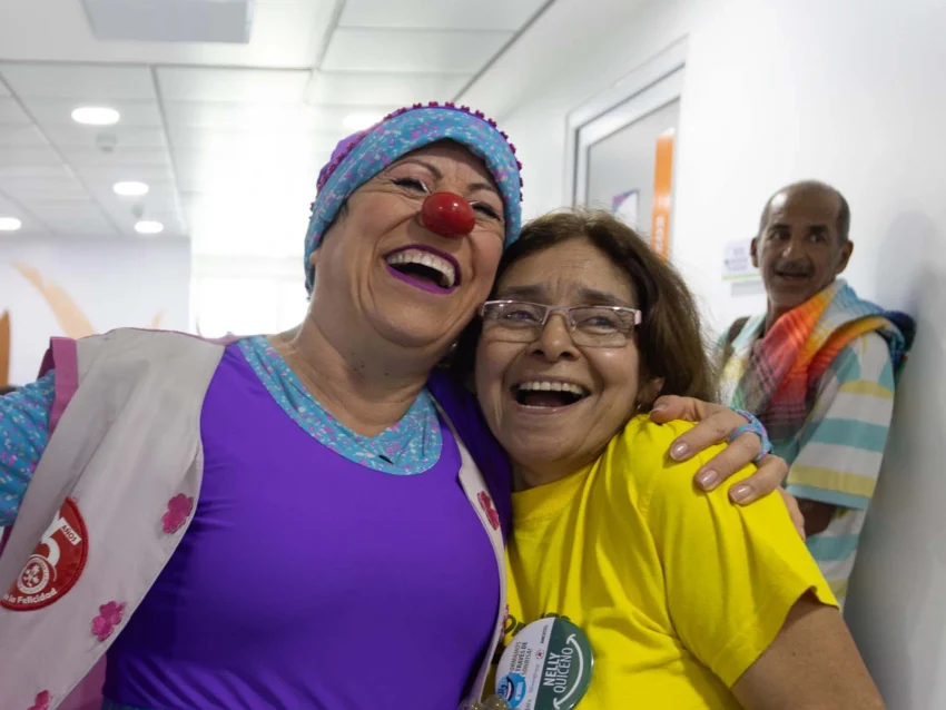 A volunteer, dressed as a clown, makes another volunteer laugh.