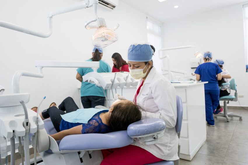 A young teenage girl lays in a dental chair while a dentist examines her 