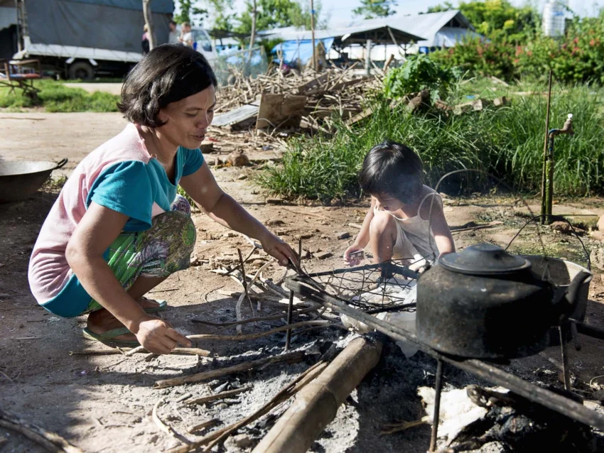 A mother and her daughter build a fire outdoors to cook their meals.
