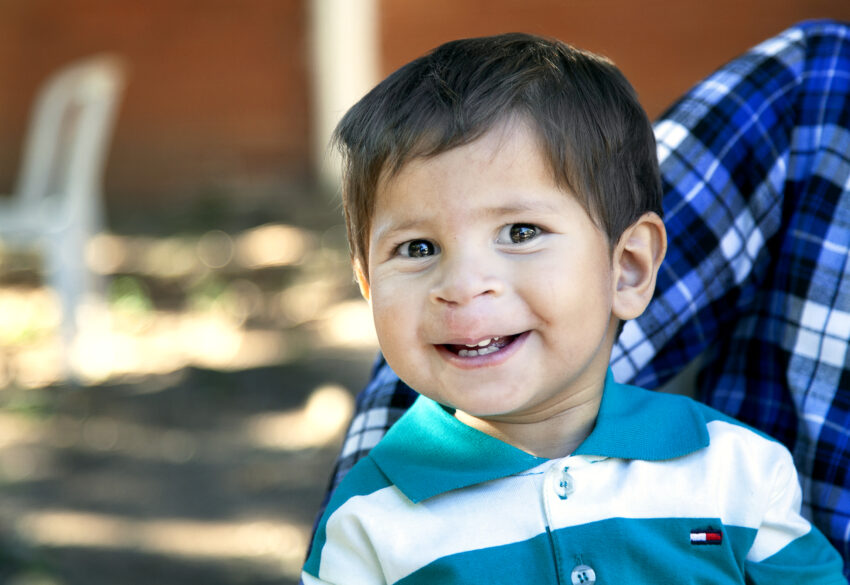 A child smiling in a blue and white shirt with a new smile after receiving cleft surgery