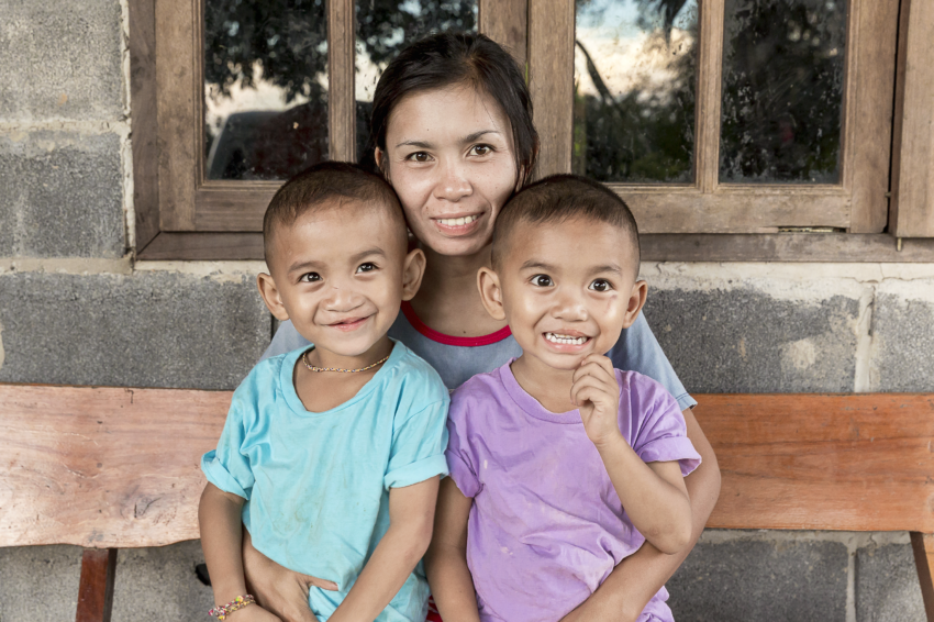 2 young boys with their mother sitting on a bench smiling