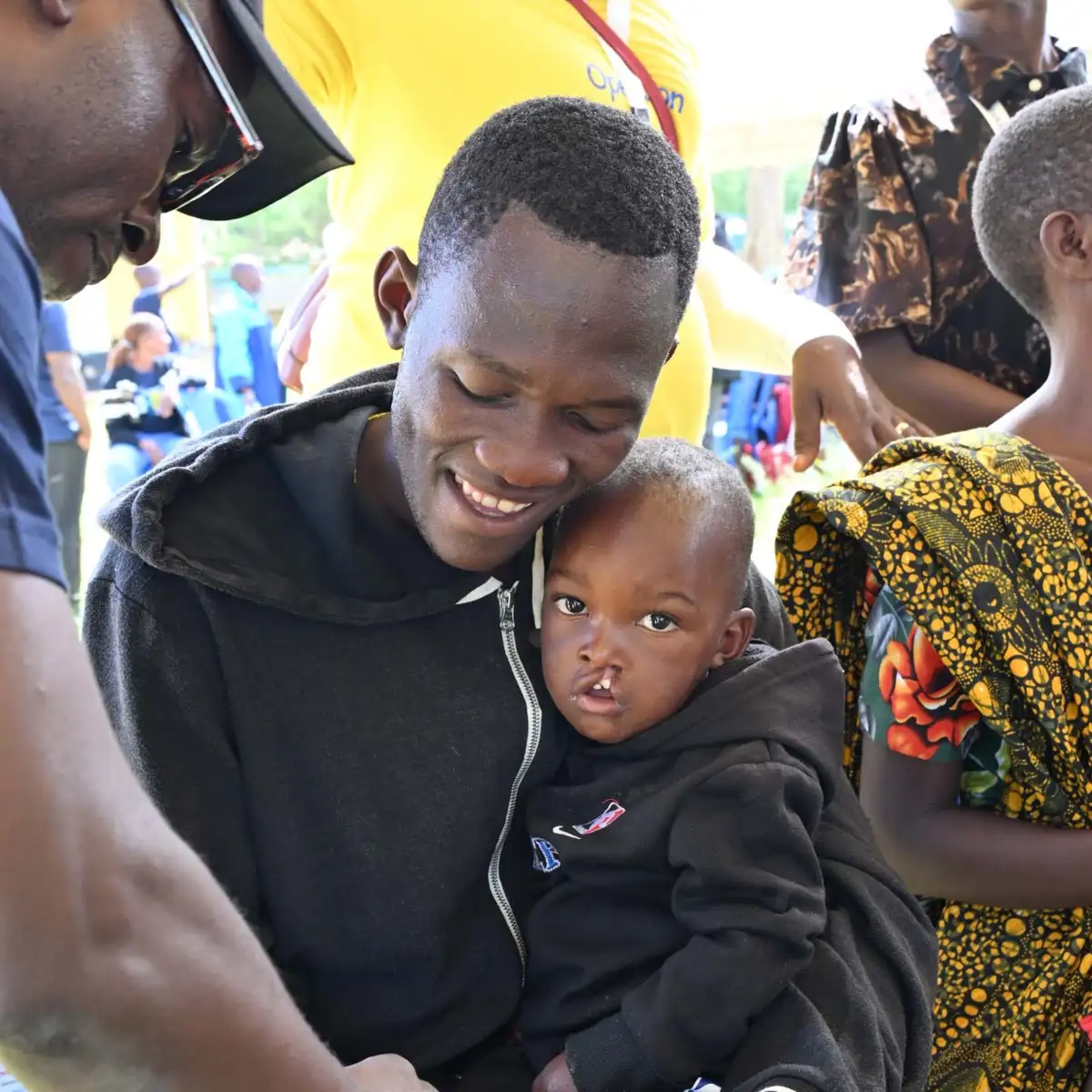 A father smiles as a volunteer prepares his son for cleft care assessments.